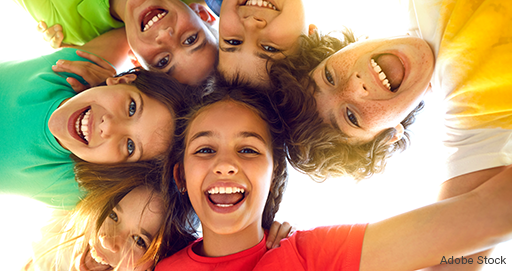 Sechs Kinder in bunten T-Shirts, die zusammen von oben in die Kamera lachen